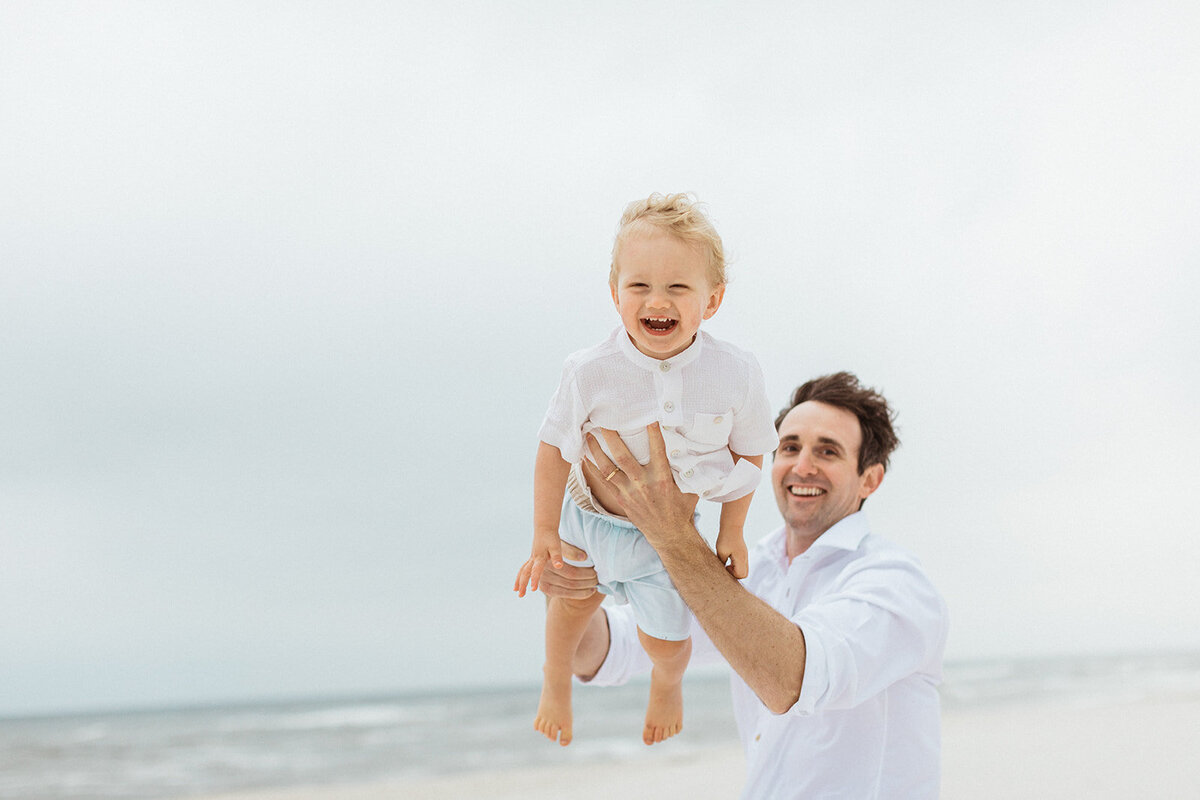 dad plays with two year old son tossing him in the air on the beach