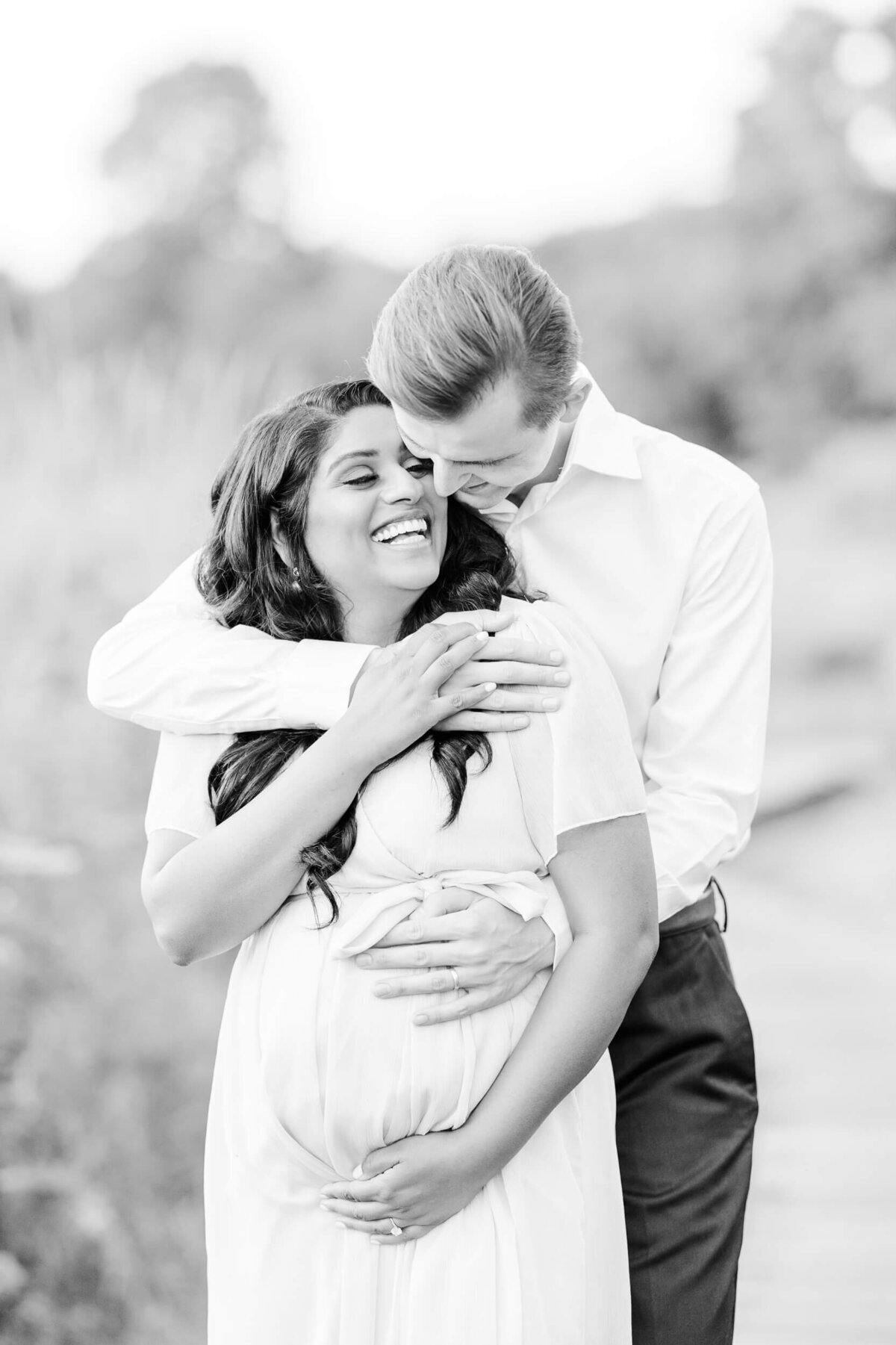 A pregnant woman and her husband smile at each other, black and white