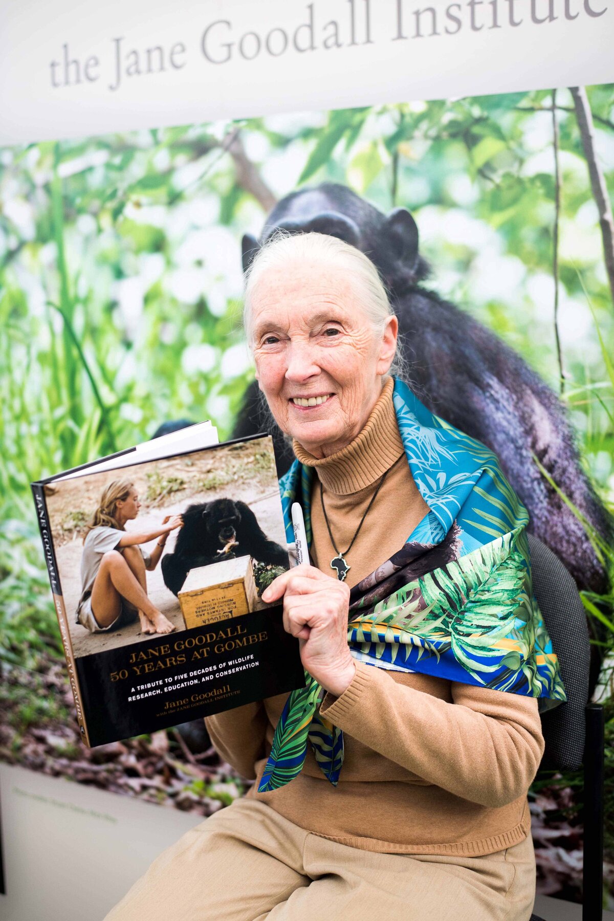 A portrait of Jane Goodall with her book smiling at the camera