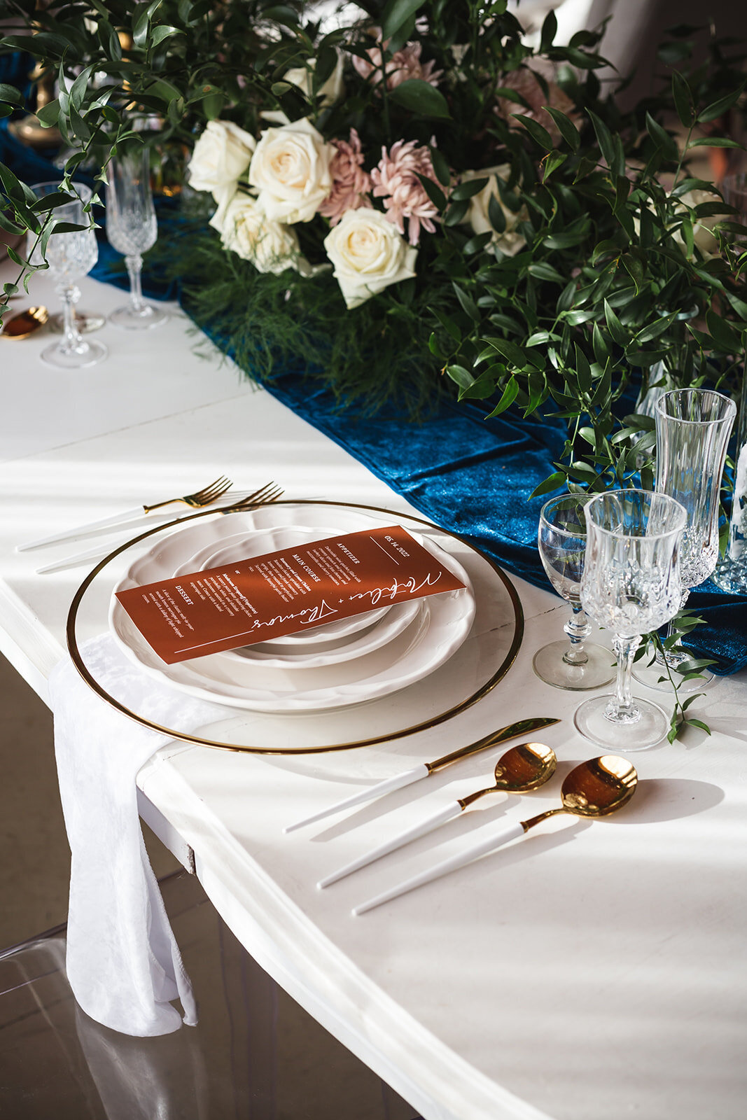 a copper menu on a white plate with a teal table runner and white roses