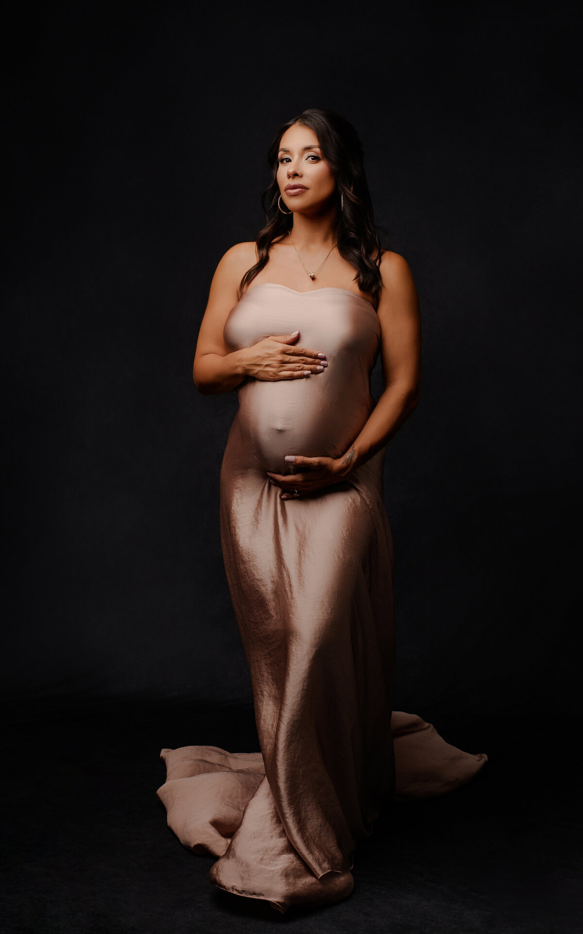 pregnant mother with hands on her belly in a satin pink dress