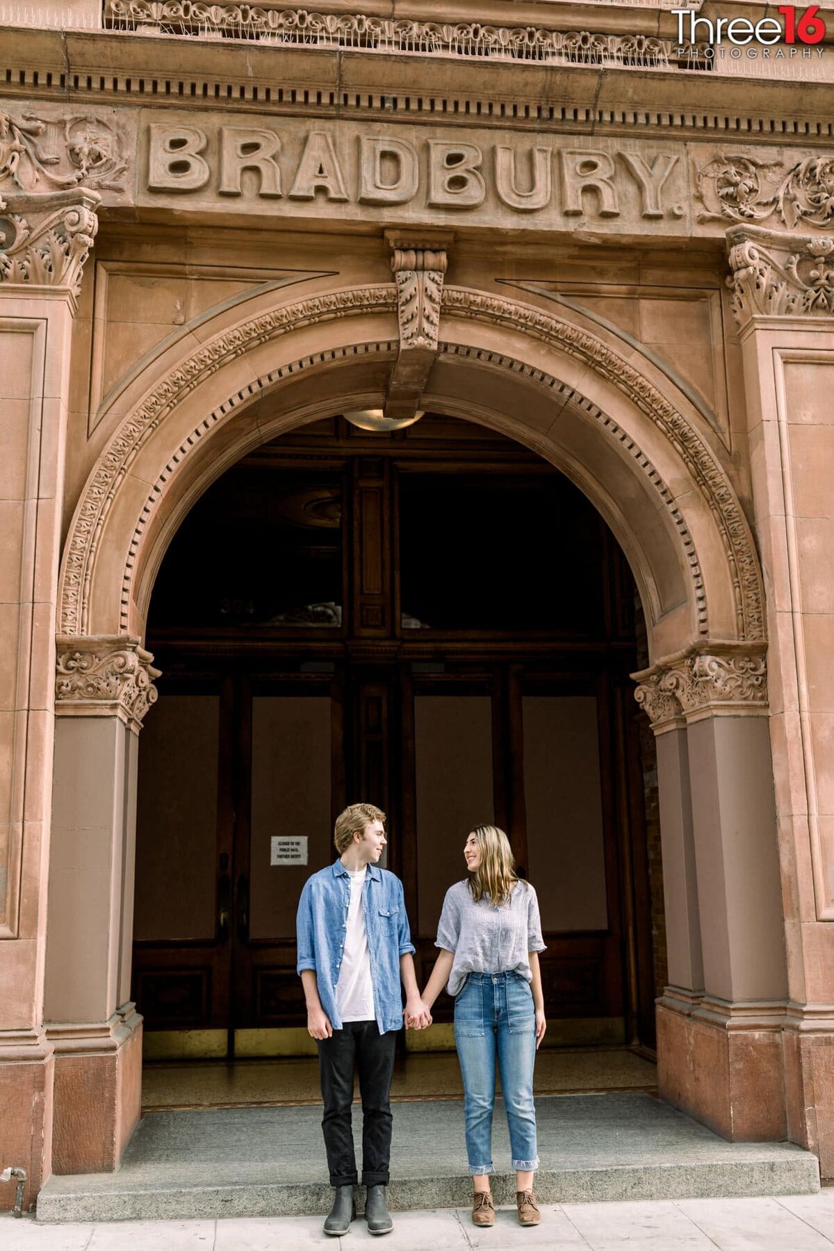 Engaged couple stare at each other while holding hands during photo session at the Bradbury Building