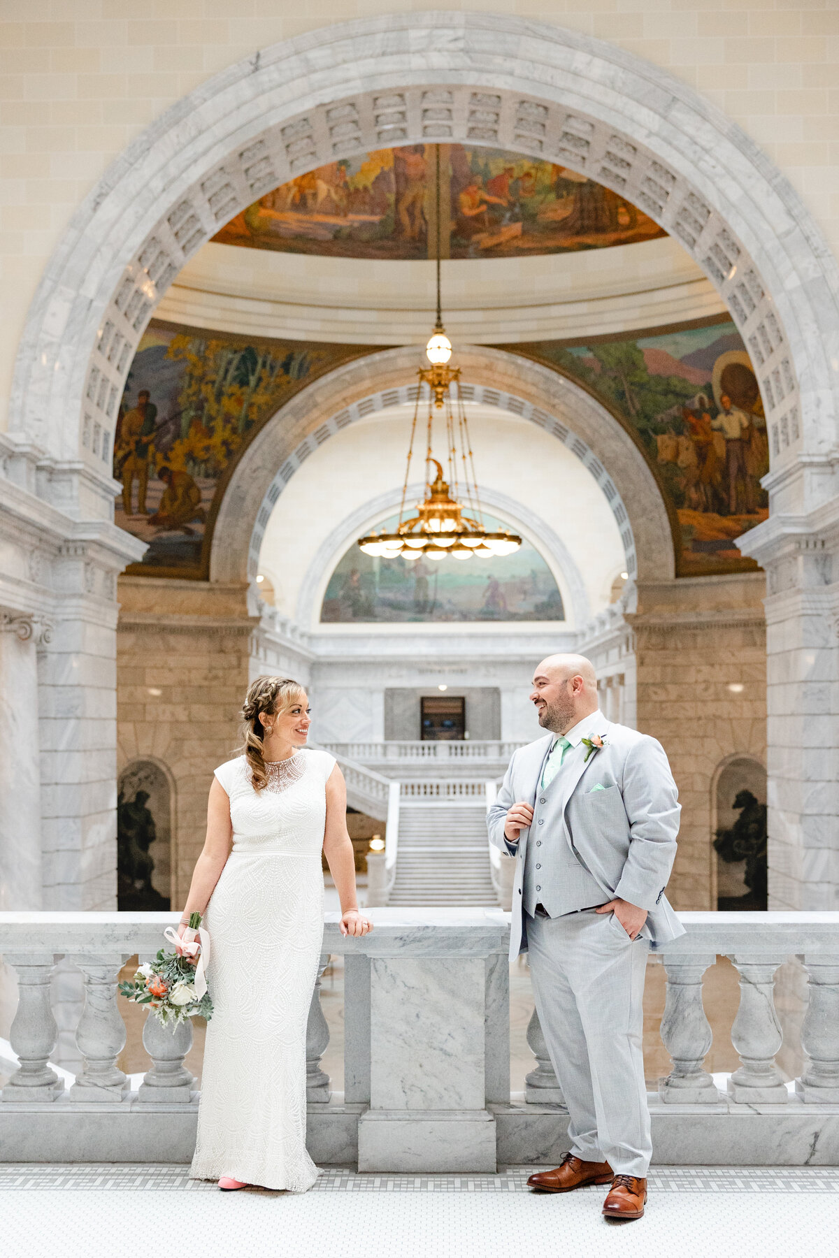 Bride and groom standing on the grand marble balcony of the Utah State Capitol, gazing into each other's eyes.
