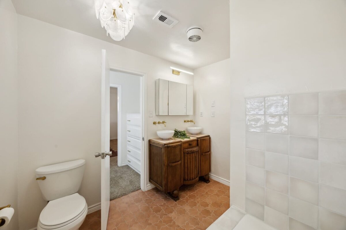 Primary bathroom at 3120 Chapel Downs Dr Dallas TX featuring vintage wood vanity with double vessel sinks and brass fixtures — Haven Realty Group.