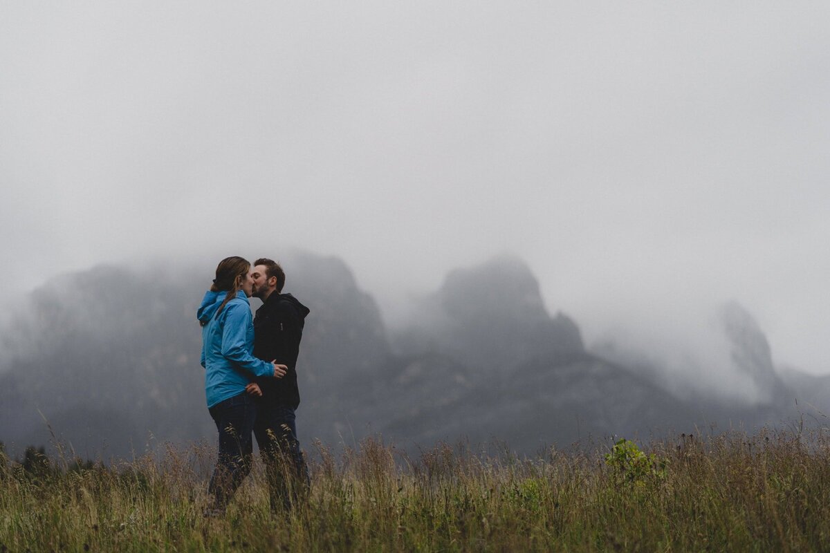 Engaged couple kissing in front of mountain 