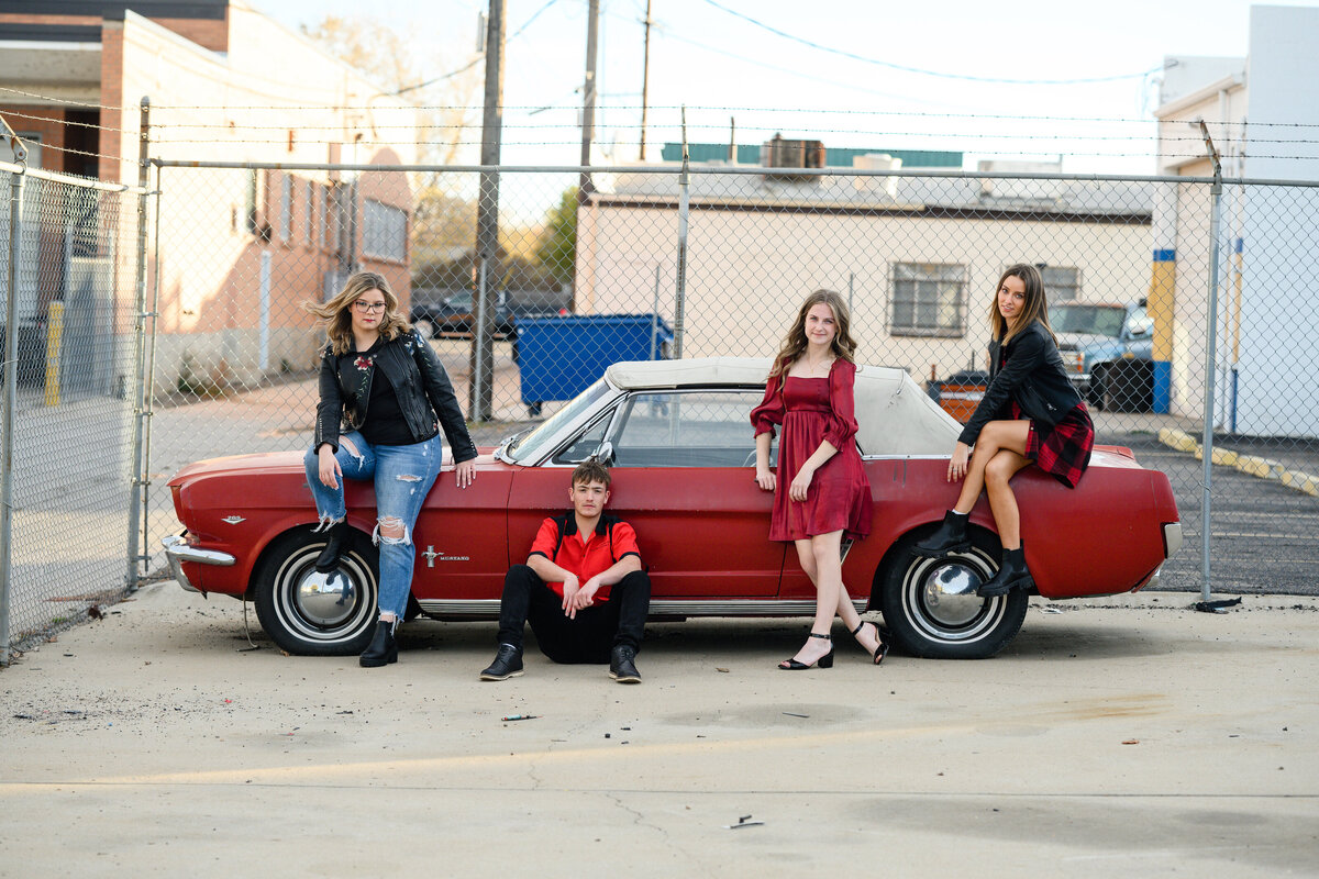 Senior picture ideas for a rep team of 4 kids in red and black sitting on and around an old red vintage car