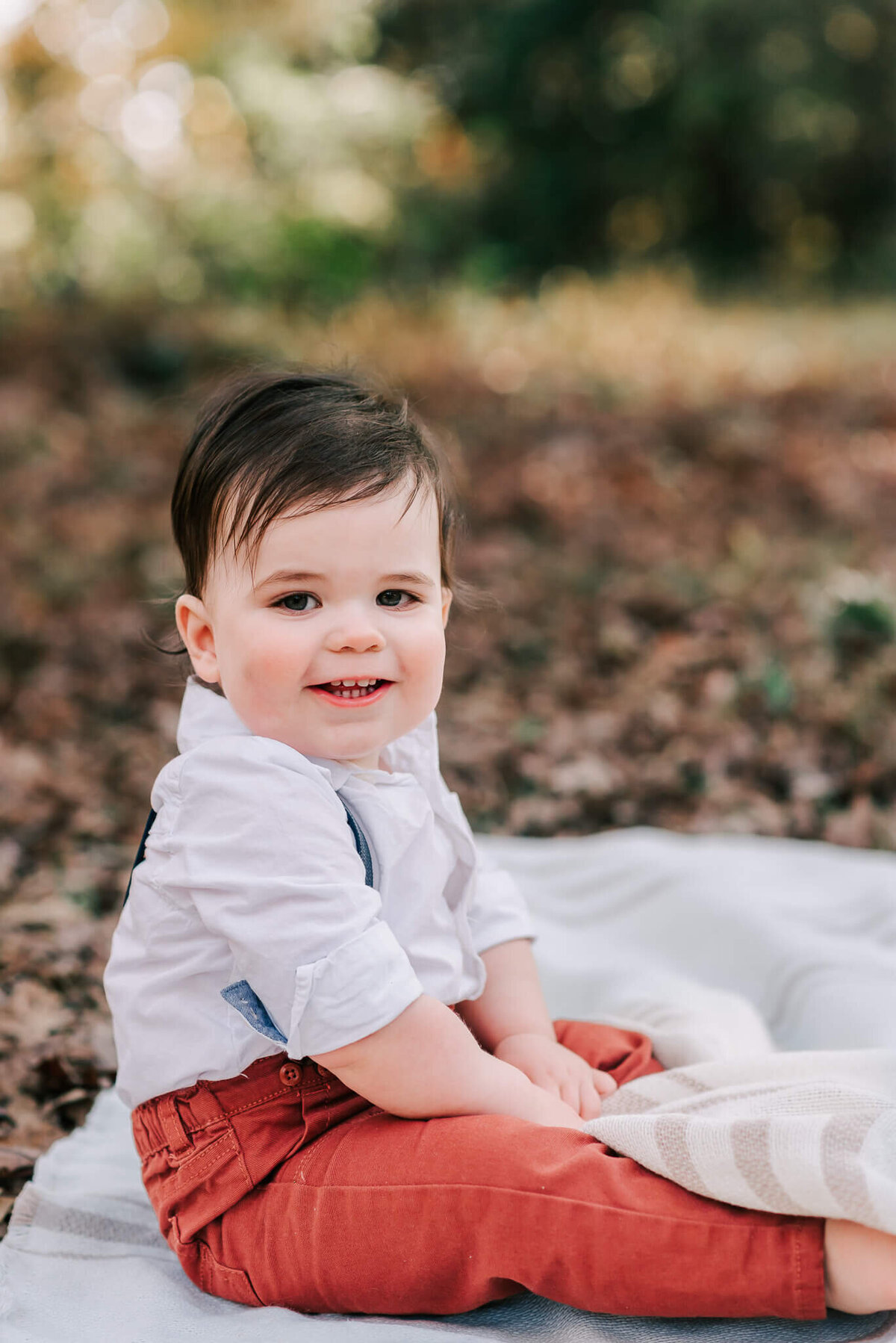A smiling boy sitting on and playing with a white blanket in Lake Fairfax Park