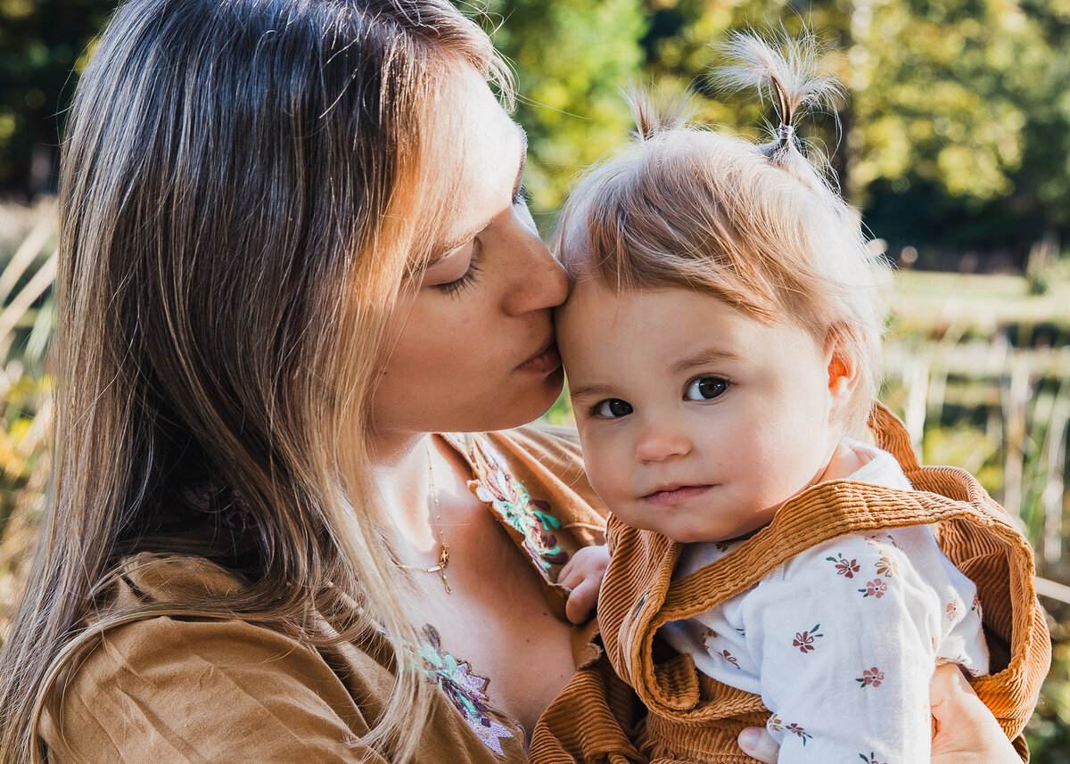 Lifestyle photo of mother kissing baby daughter at a Union County, New Jersey park in the fall.