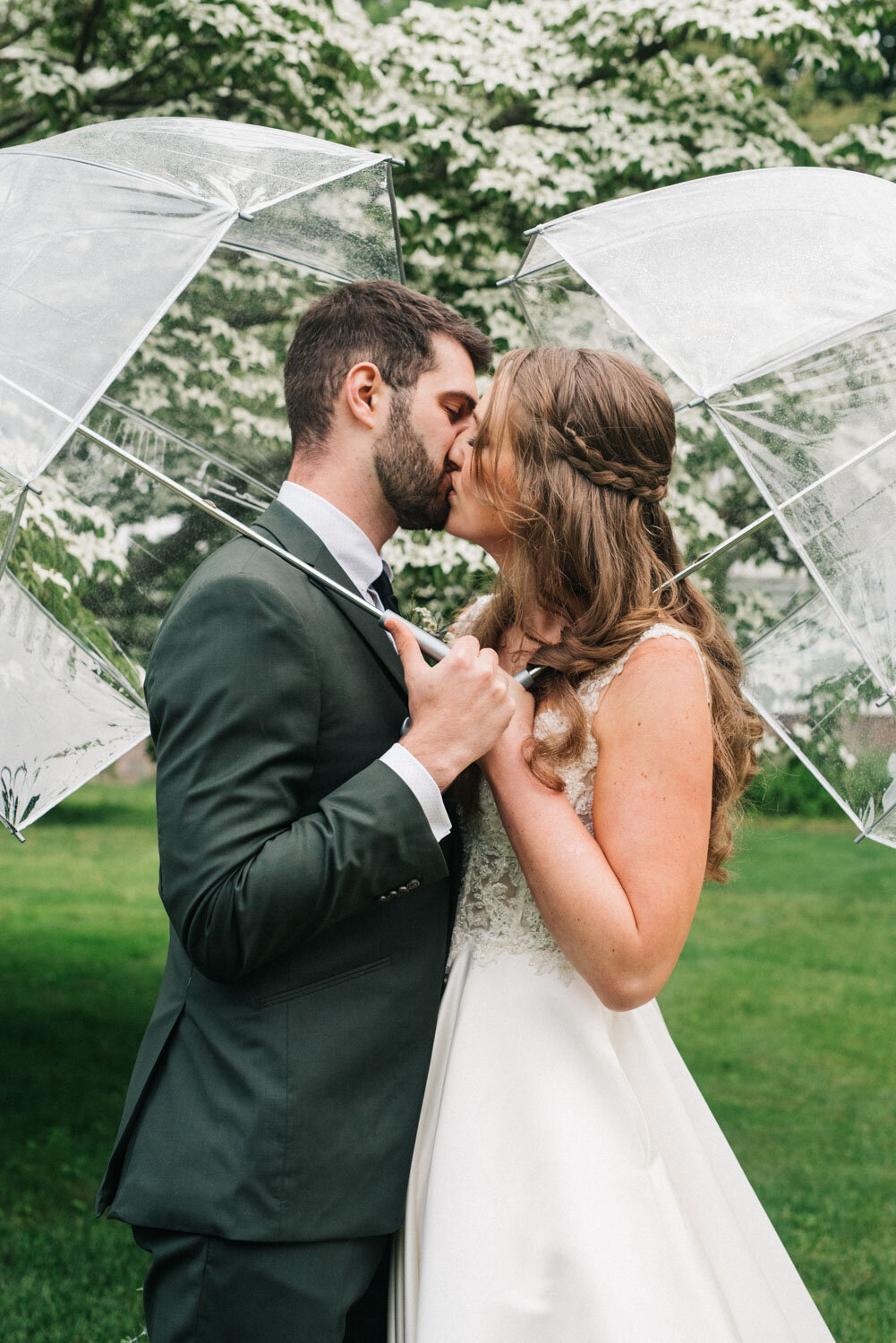 Bride and groom both holding a clear umbrella kissing
