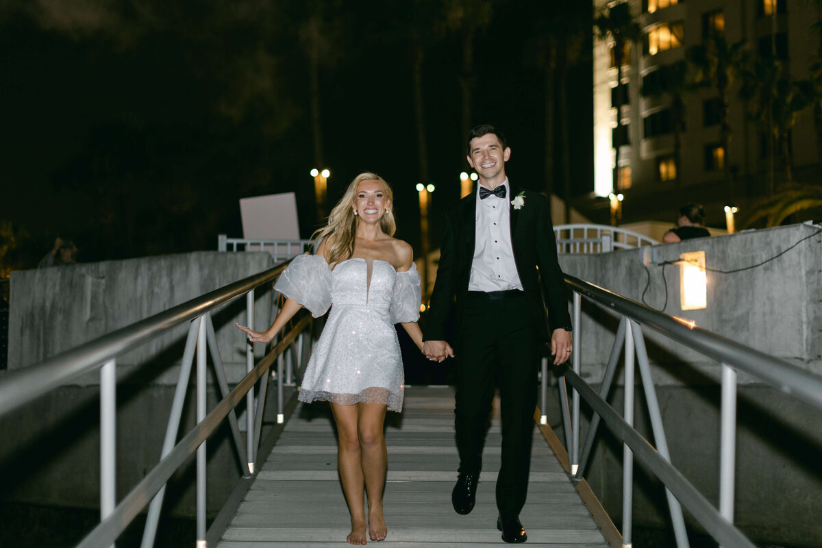 A bride and groom walk down a gangplank at night.