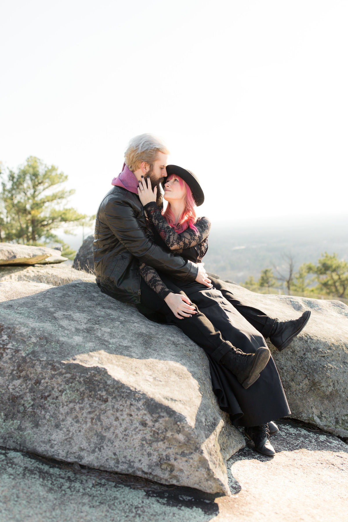 trendy engaged couple with pink hair holding each other on Stone mountain for photograph