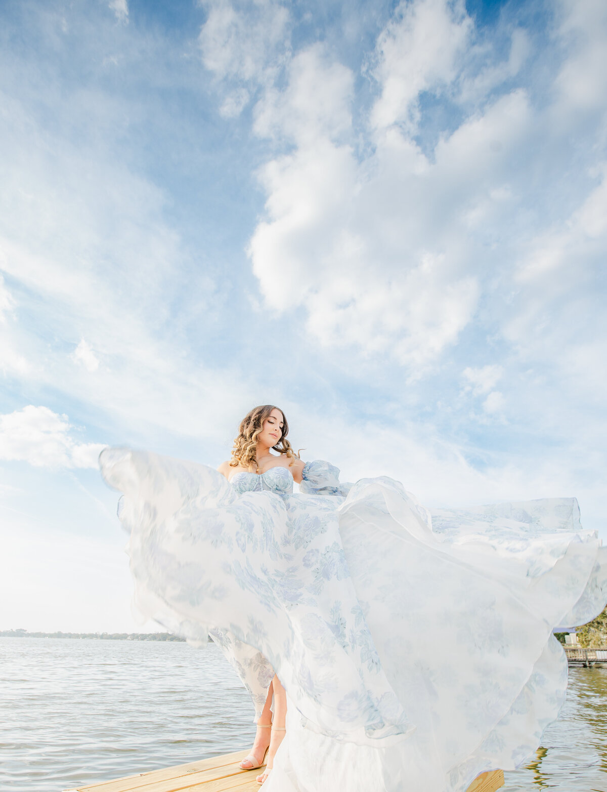 Bride with flowy dress near the water moving around with beautiful sky in the background, happy