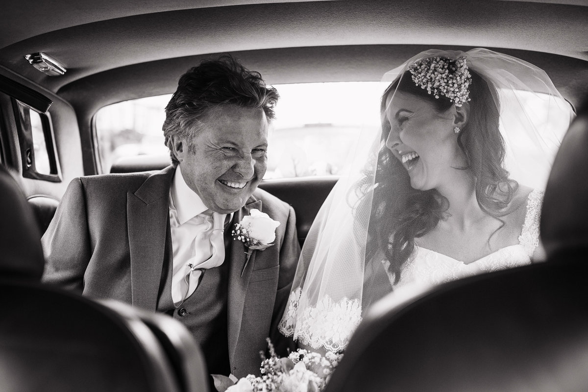 Bride and her dad laughing in the wedding car on the way to the ceremony