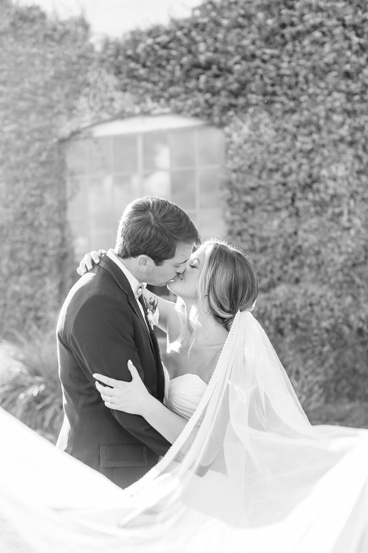Black and white portrait of bride and groom kissing with the veil cascading out towards the camera at Olde Dobbin Station