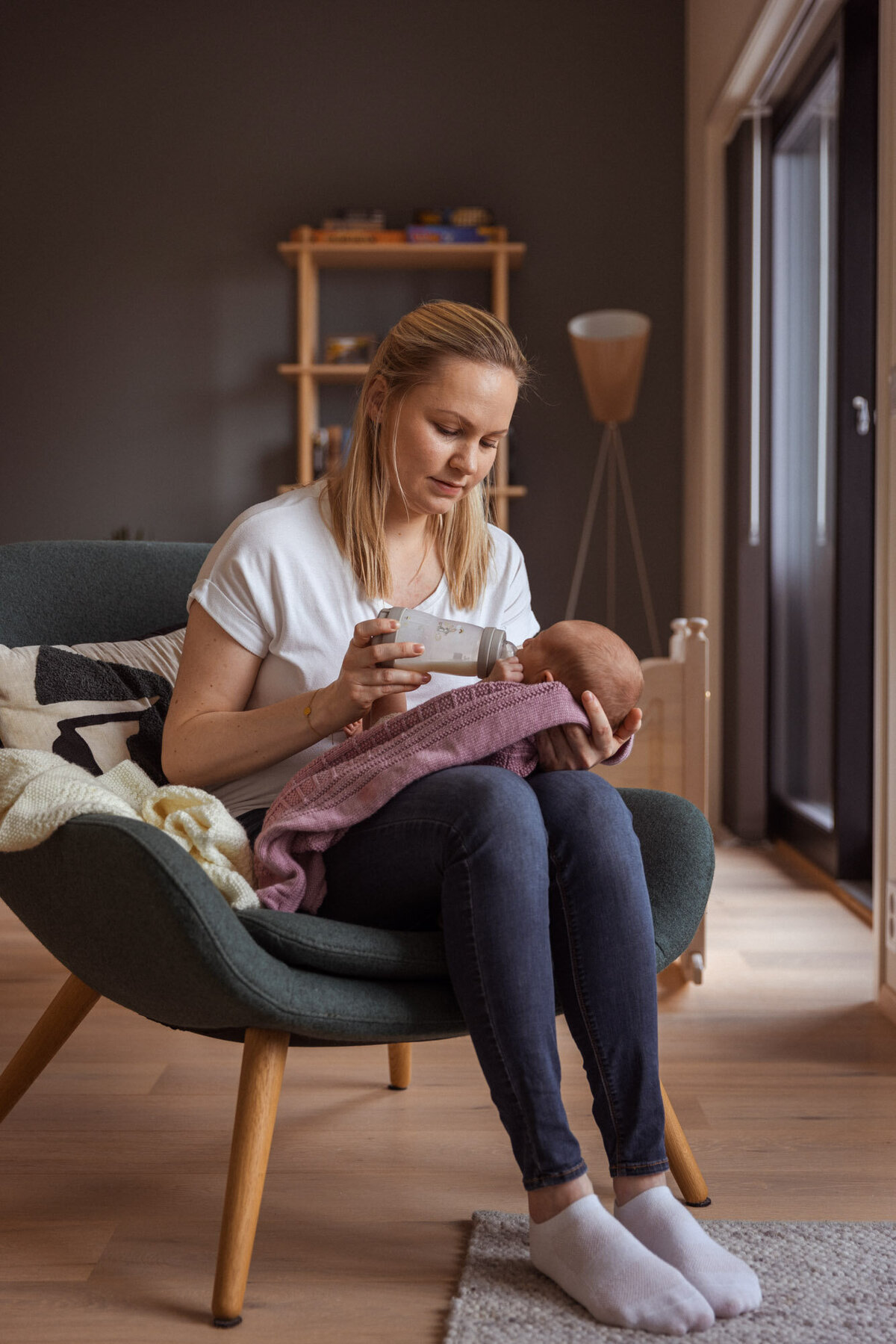 Livsstilsfoto av en mor som sitter i en lenestol og flaskemater babyen sin.