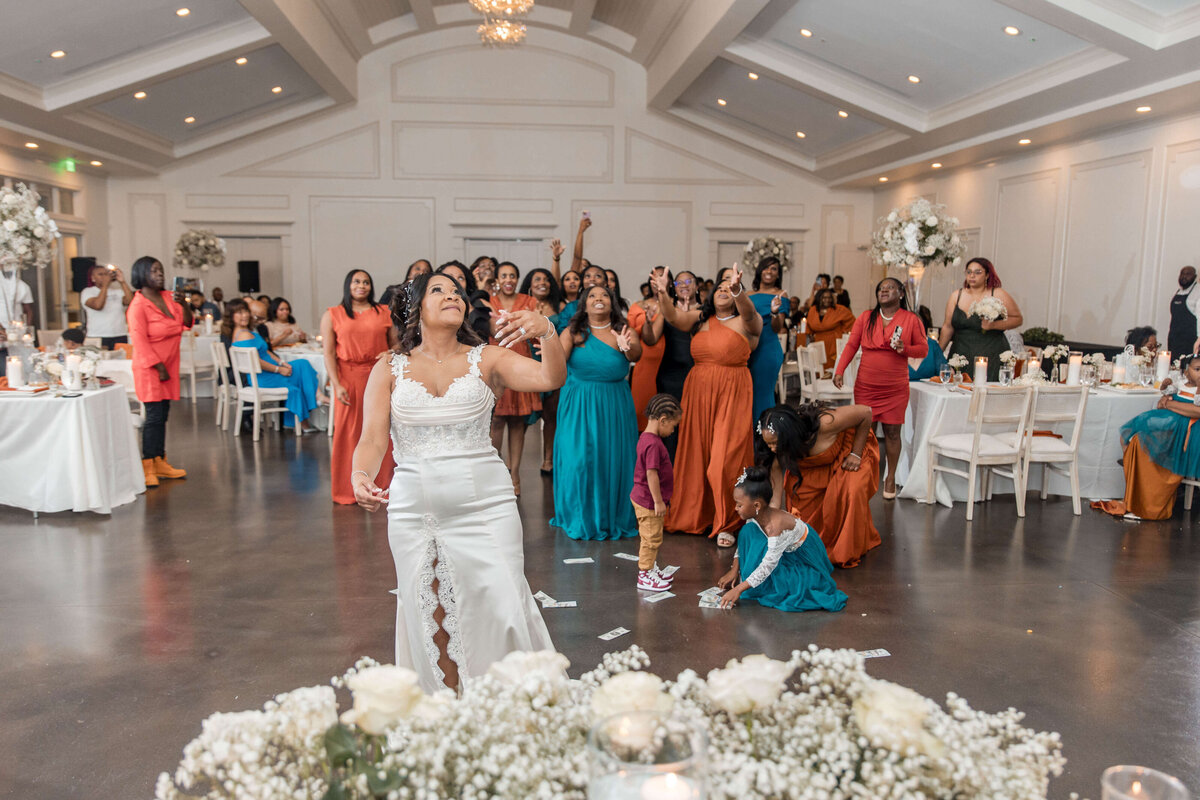The bride joyfully throws her bouquet into the air as bridesmaids and guests eagerly reach for it.