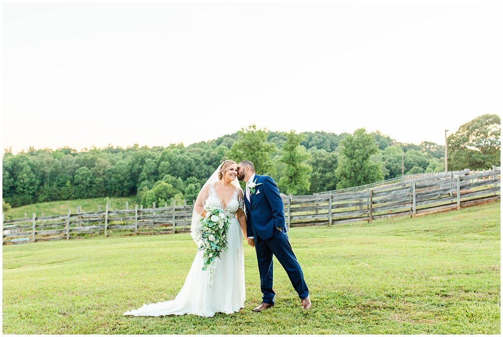 groom kissing bride on cheek in a field