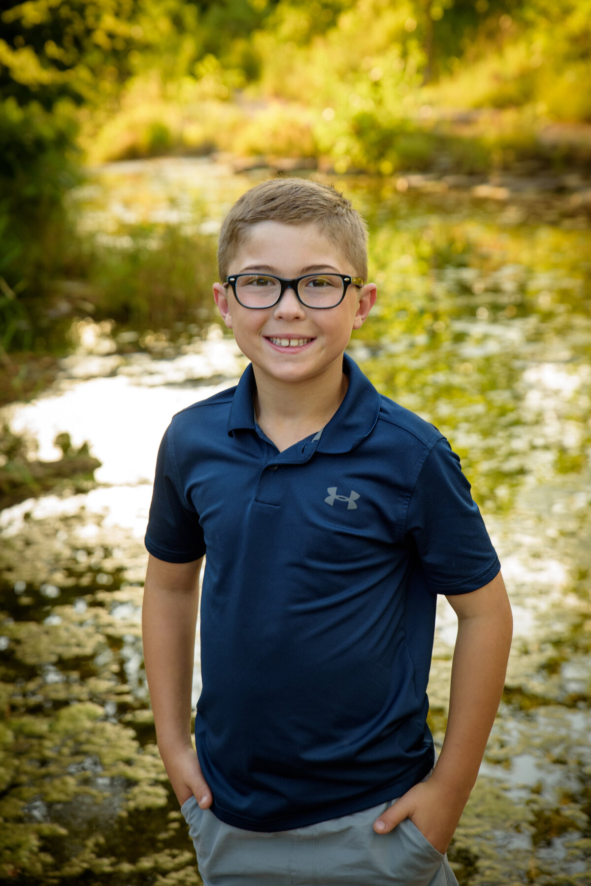 Young boy wearing glasses and a navy polo shirt standing near the creek at Fonferek Glen County Park near Green Bay, Wisconsin