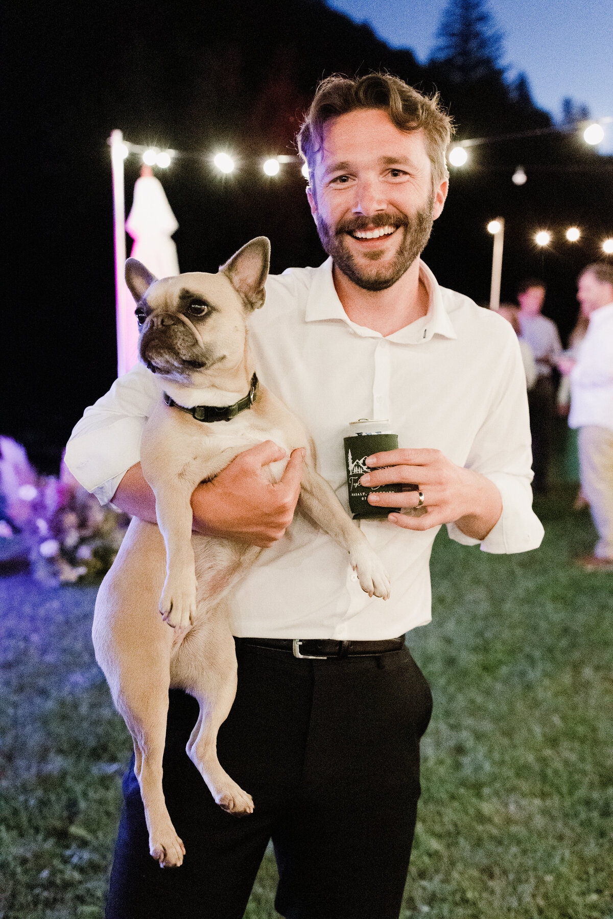 Man holding a dog and a drink at outdoor wedding reception at Dallenbach Ranch Colorado