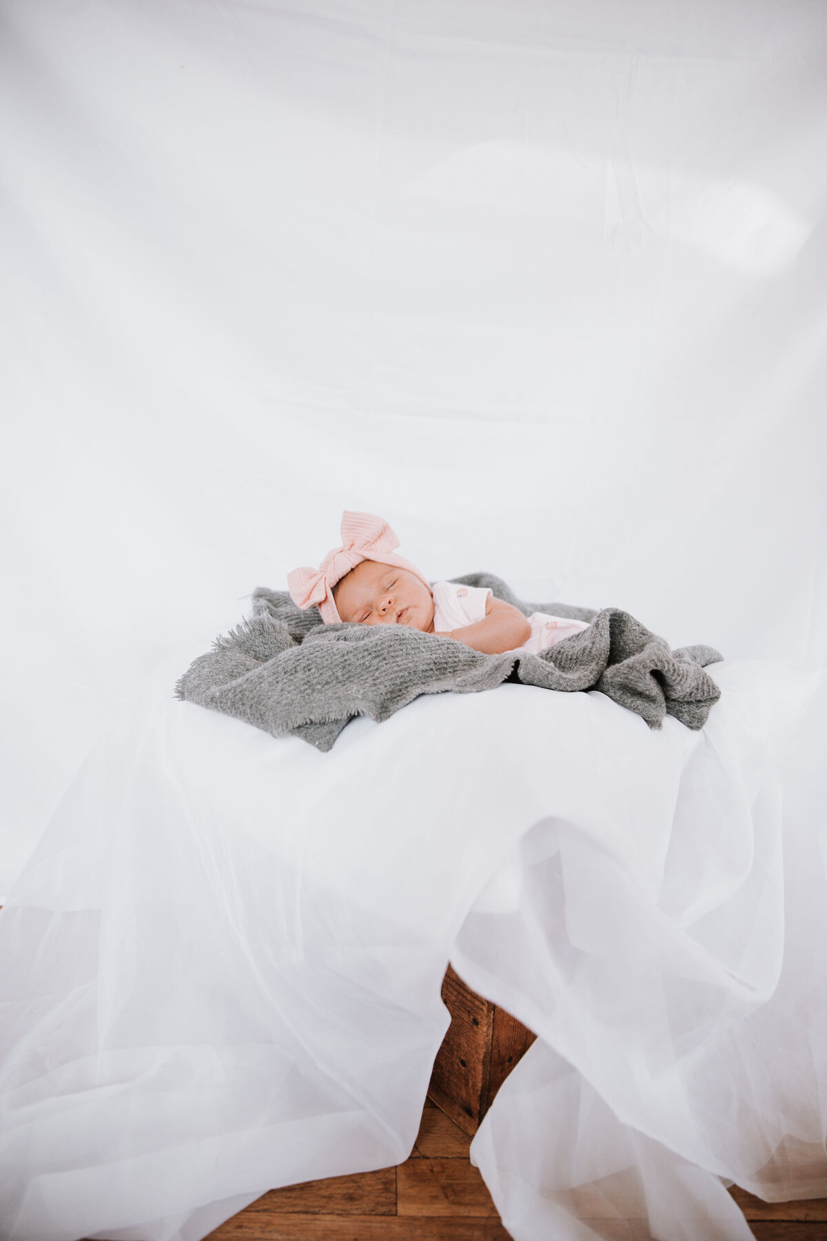 in studio newborn photos in Idaho Falls with baby girl laying on a grey swaddle while wearing a pink bow on her head