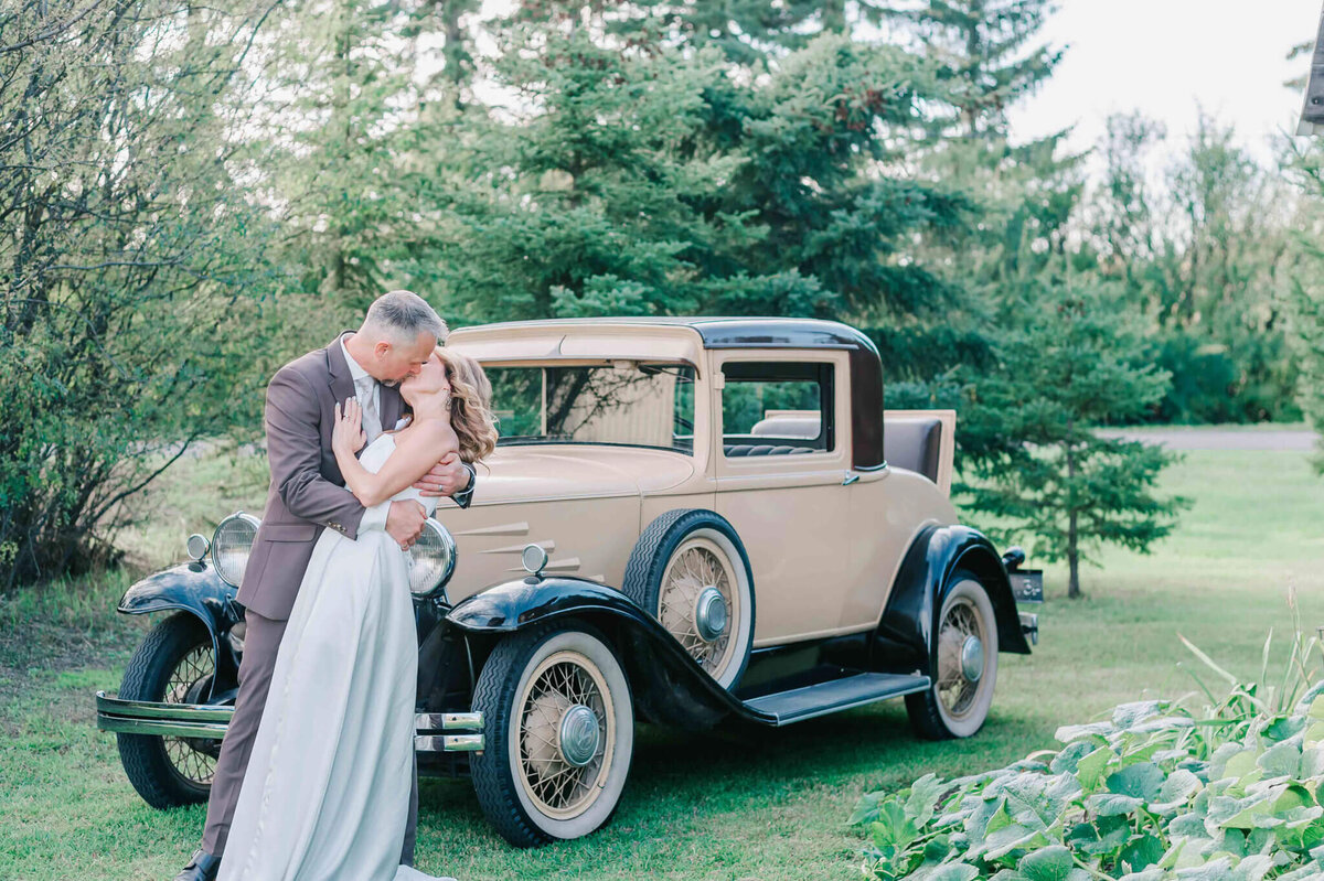 bride and groom having a kiss by a 1930's plymouth.