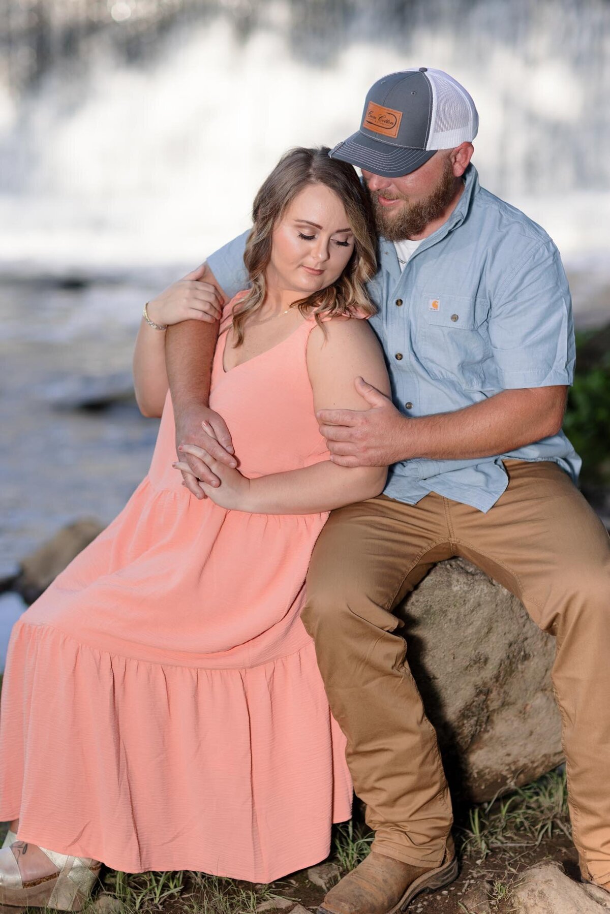 Sweet couple sitting in front of a waterfall cuddling on a rock.