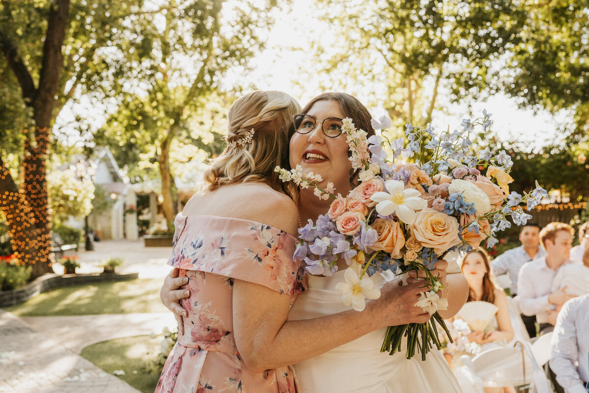 A person hugging a newlywed who is holding a bouquet of flowers 