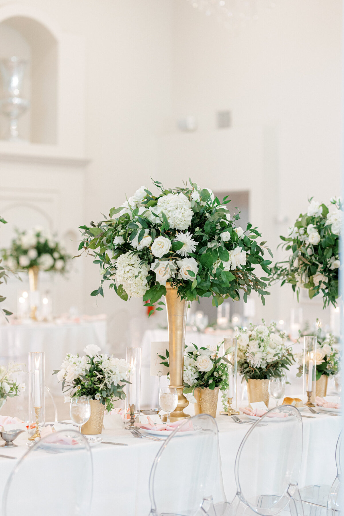 reception venue table settings and tall centerpieces with gold vases white flowers and greenery