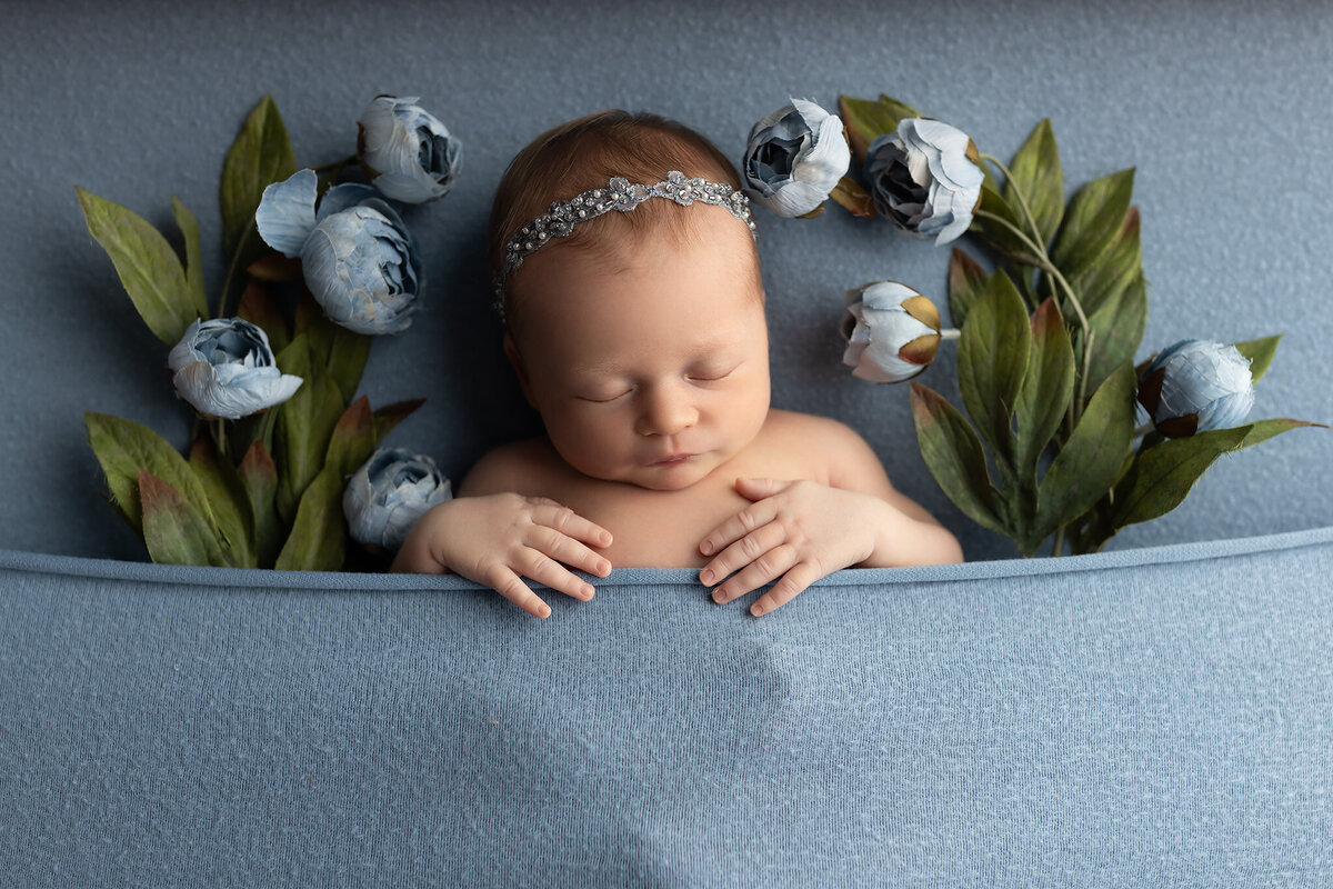 Newborn baby girl tucked in with soft blue florals during a luxury newborn photography session in Dallas.