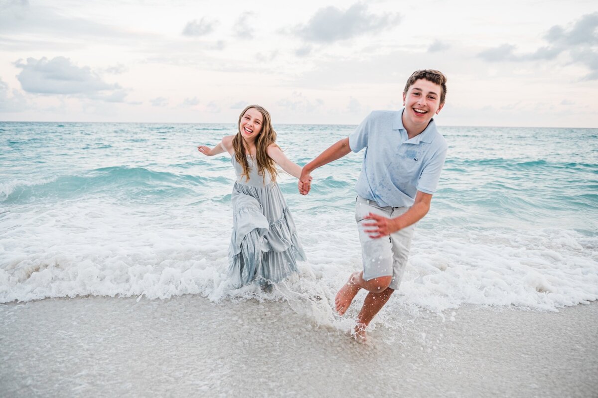 brother and sister holding hands run out of ocean  at Pensacola Beach