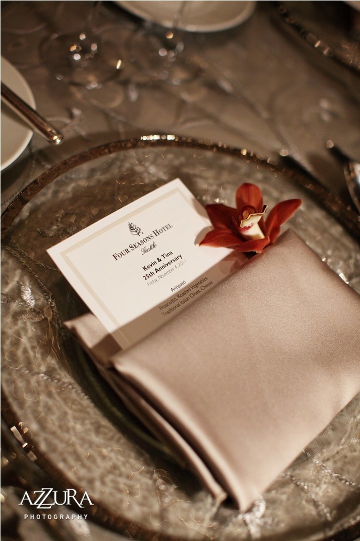 place setting for an elegant anniversary party with silver napkin, silver rimmed glass charger plate, and red orchid