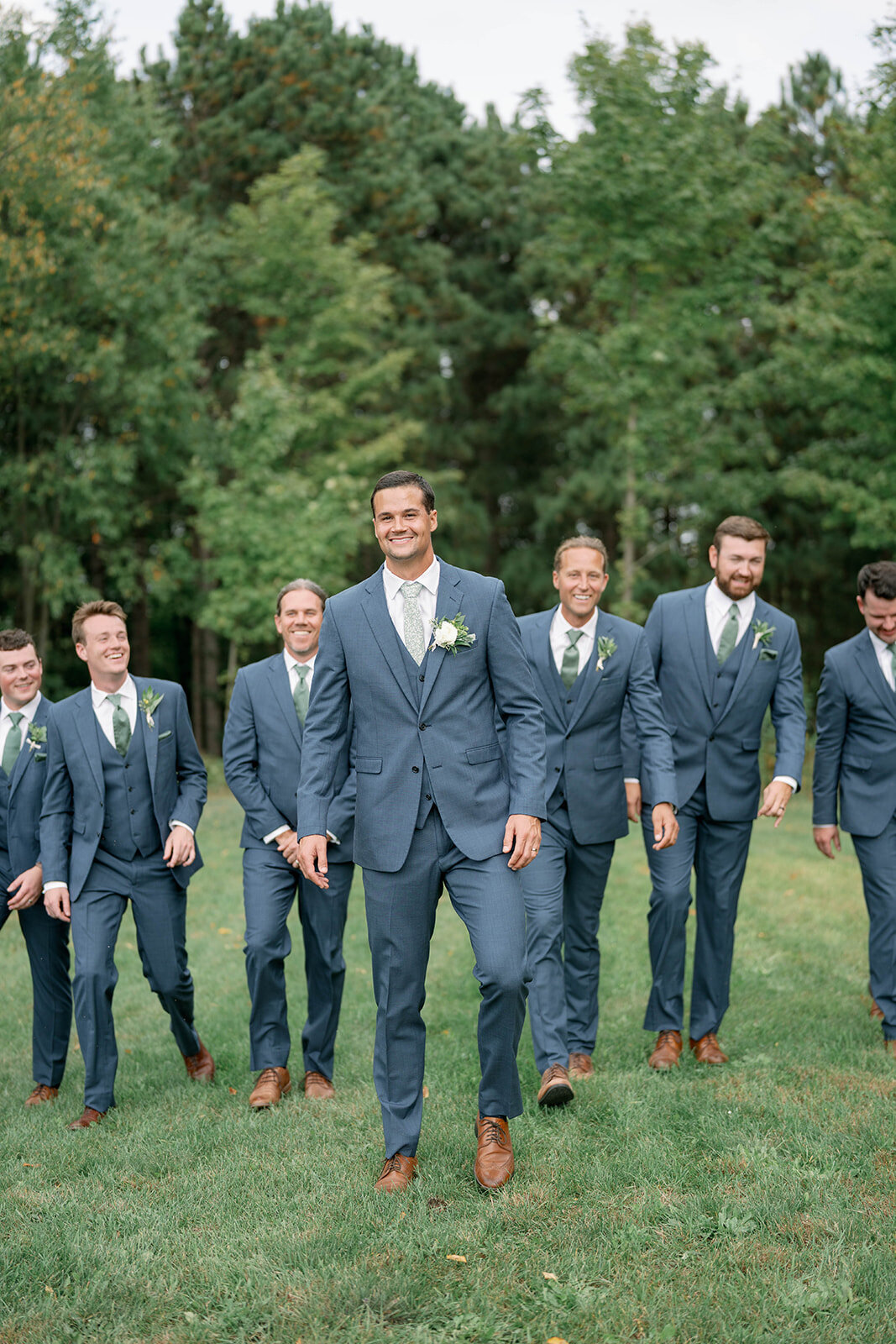 All the groomsmen walking together laughing during outdoor portraits at The Cherry Barn in Frankfort MI.