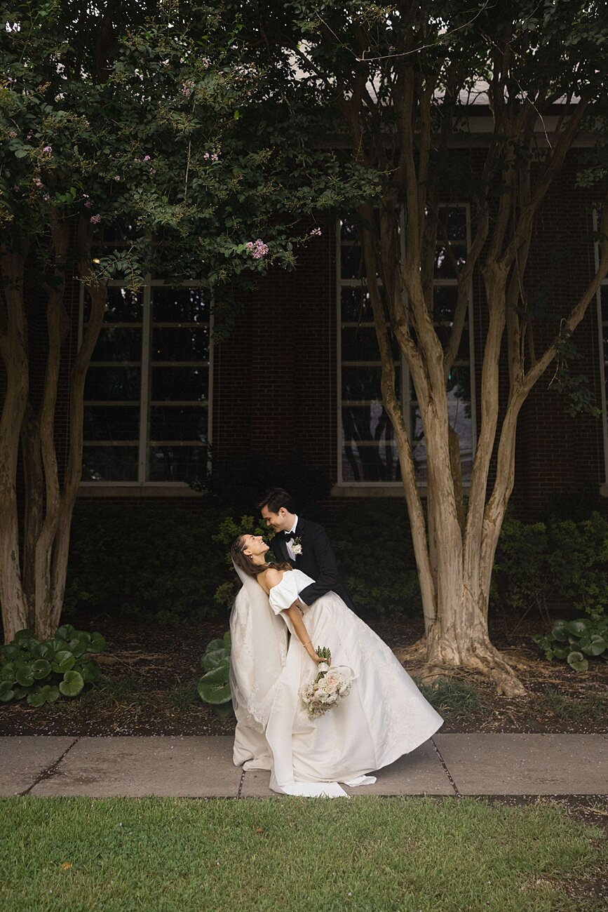 groom kisses bride as he dips her back on the side of a church
