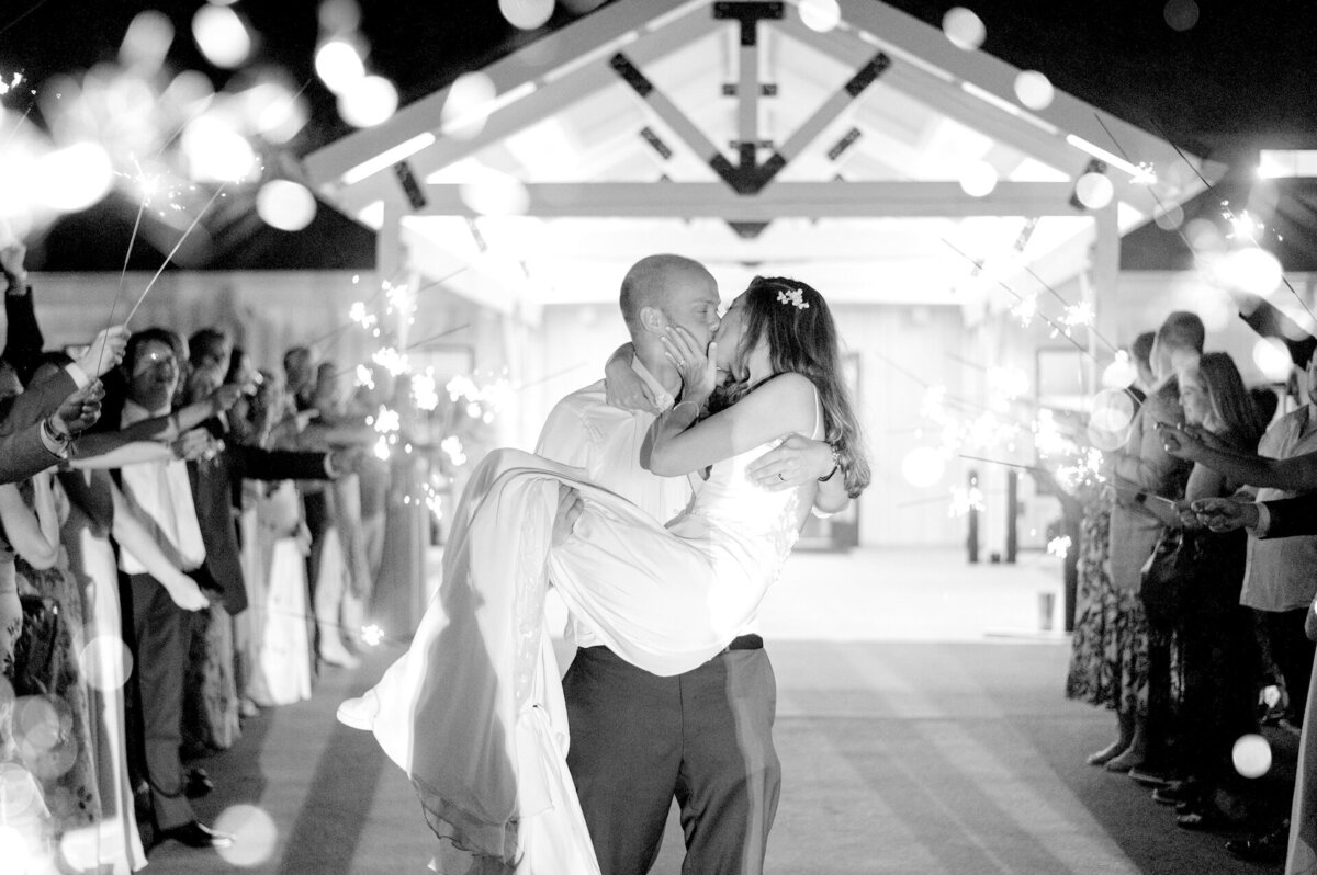 bride and groom kissing as they exit their wedding while guests hold out sparklers