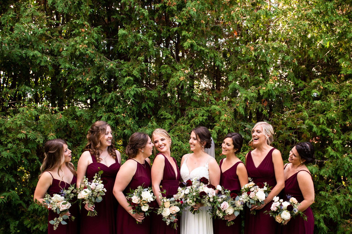 Ottawa wedding photography showing bridesmaids in burgundy dresses laughing together taken outside the Marshes wedding venue