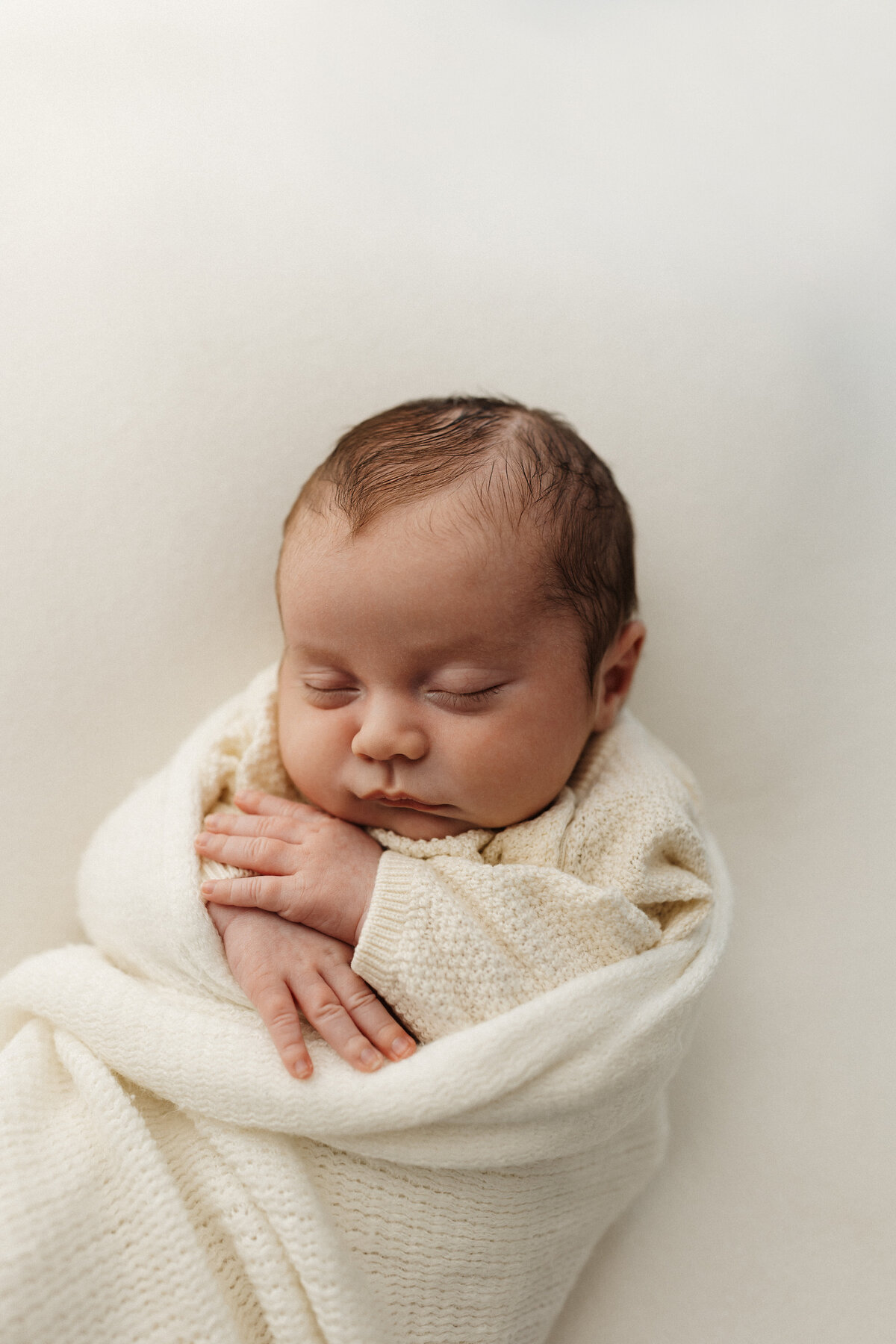 a newborn baby with beautiful long hair being posed by christchurch newborn photographer lucy jane photography