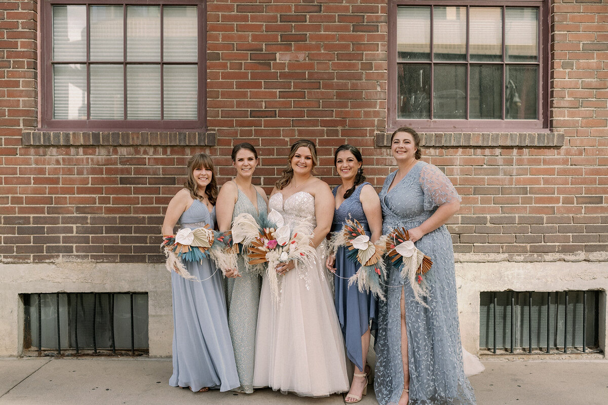 Bride poses with her bridesmaids in dusty blue dresses.