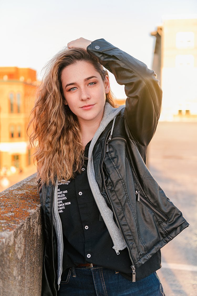 High school senior girl in black leather jacket on rooftop of parking garage with sun in background