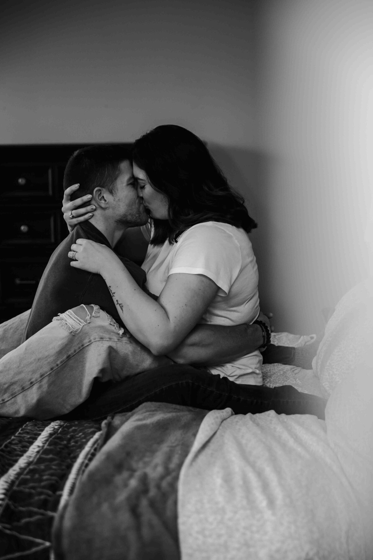 husband and wife sitting in bed kissing, seen through the doorway in black and white