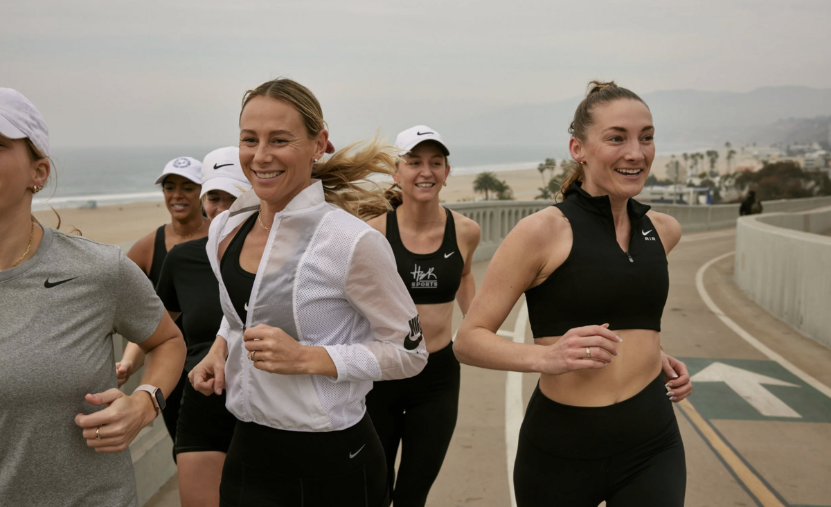 HER Sports Club runners jogging together along the beach path, smiling and training as a supportive women’s community.