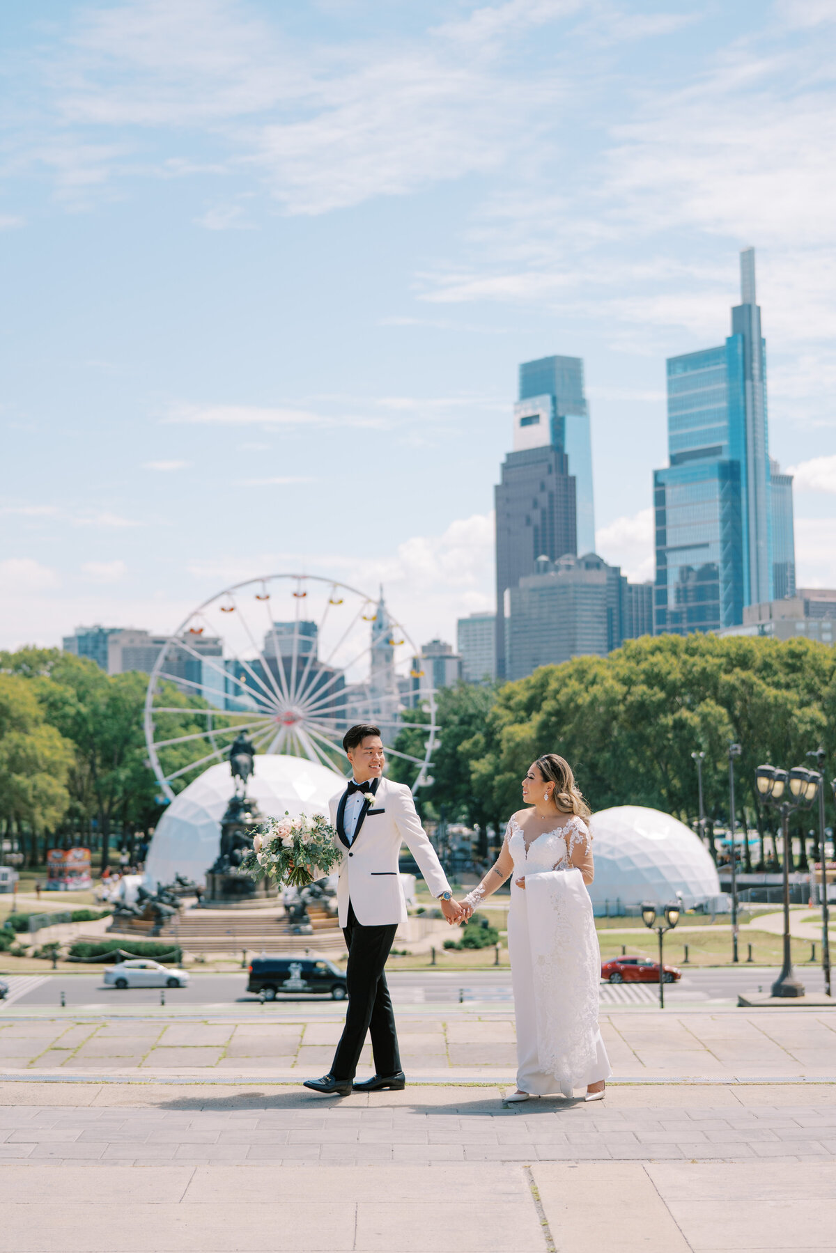 Bride and groom walking and holding hands outside at the Philadelphia Art Museum with the city in the background.