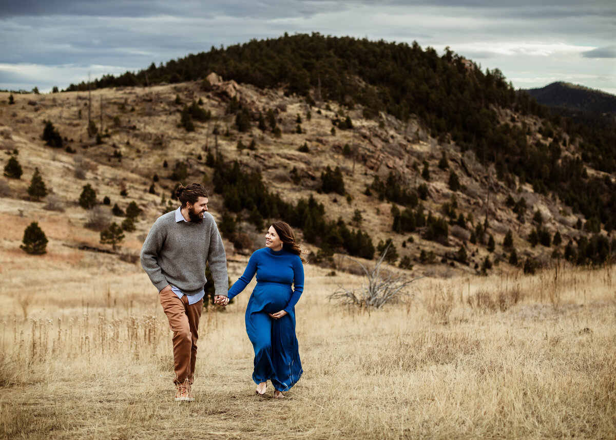 Expecting couple walking in a field in Colorado mountains during maternity photoshoot by Denver photographer Erin Jachimiak