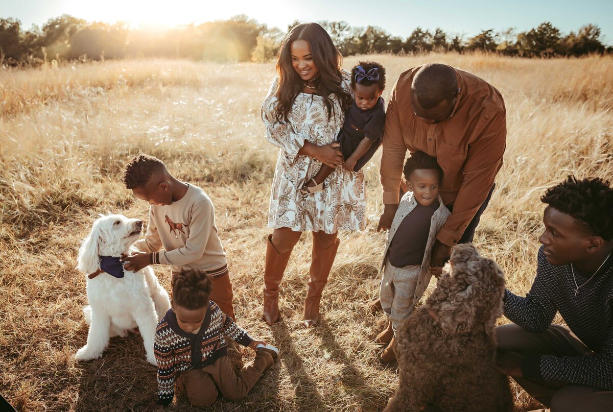 a family of seven and their two dogs are posing for a family session. they are having fun and smiling while playing with their dogs.