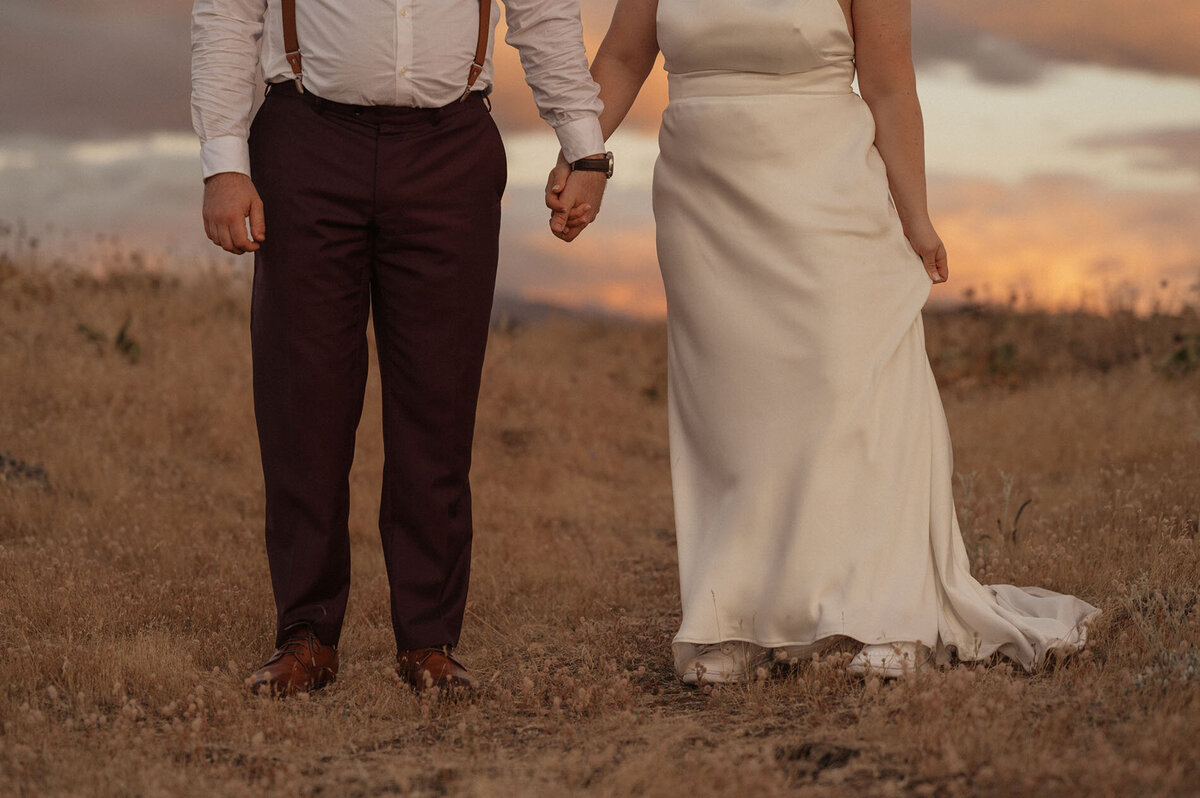 elopement couple holding hands in their wedding attire under the pink sunset sky in the Dalles, Oregon