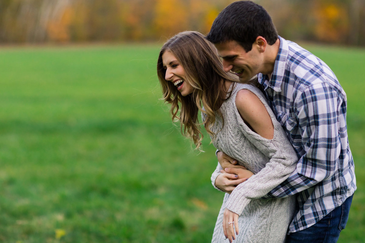 The laughing couple holds each other close at their fall engagement session with laughter at The Preserve at Chocorua NH