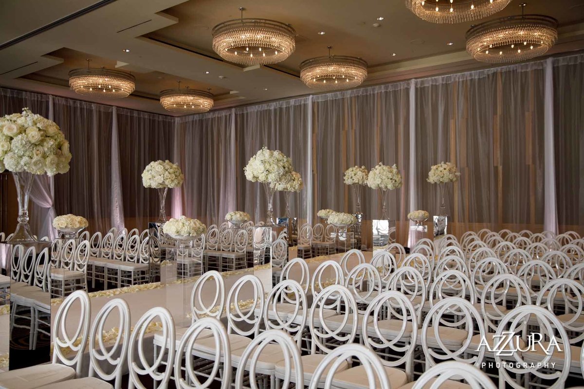 white on white wedding ceremony at Four Seasons with draped ballroom walls, white chairs, and large white floral arrangements