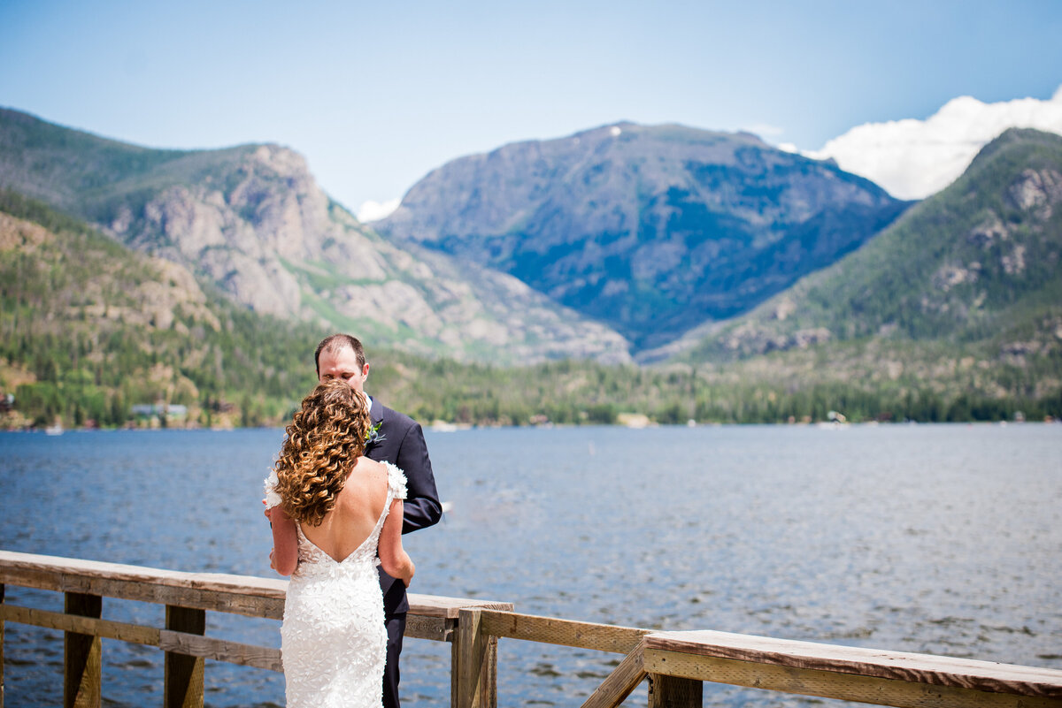 A bride and groom look into each other's eyes with a vast Colorado mountain and lake landscape in the background.