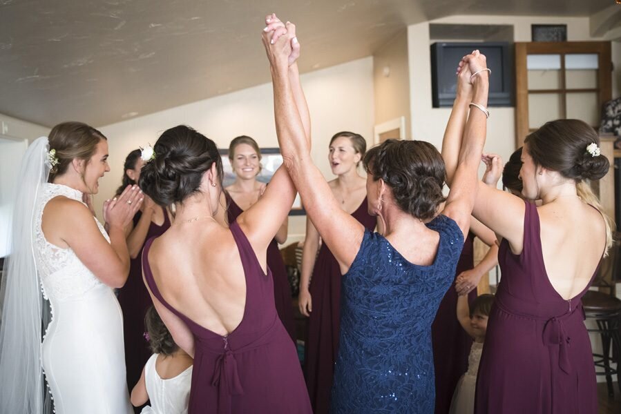 A group of bride and bridesmaids hold hands and lift them up in celebration.