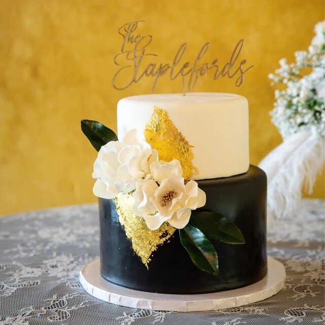 black, gold, and white wedding cake decorated with open roses and magnolia flowers