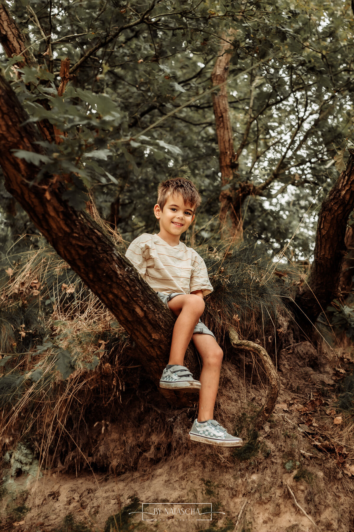 Jongen posseert lieflachend op de foto op een boomstronk bij de Bedafse Bergen in Uden